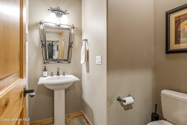 half bath with toilet, baseboards, and a sink