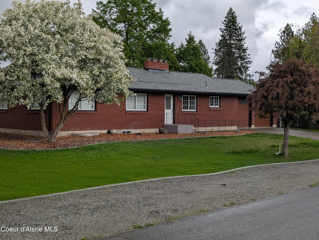 ranch-style house featuring brick siding, a front lawn, driveway, and a chimney