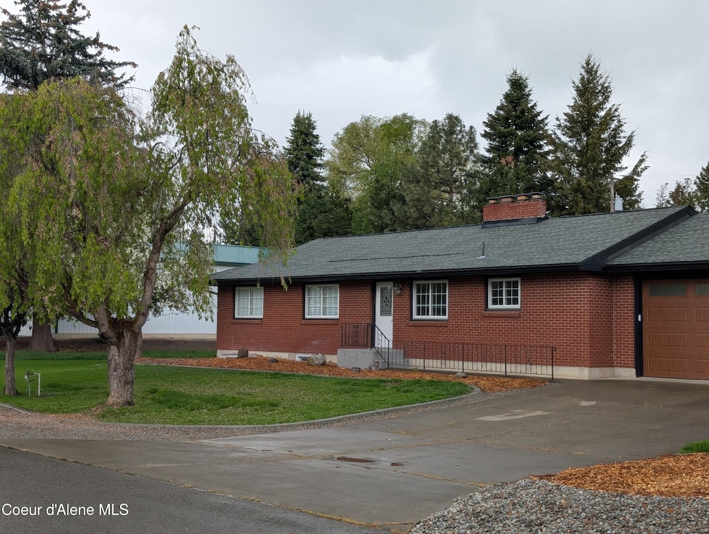 single story home with concrete driveway, brick siding, a front lawn, and an attached garage