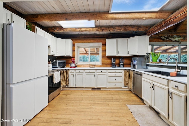 kitchen with stainless steel appliances, a sink, a skylight, light wood-style flooring, and beamed ceiling