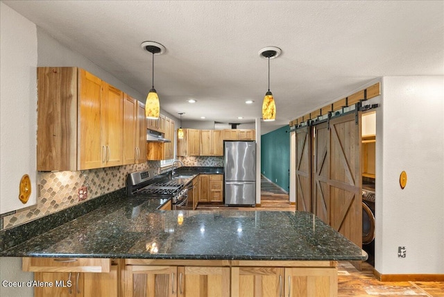 1072 Upland Dr, Sandpoint, ID 83864 - kitchen featuring appliances with stainless steel finishes, under cabinet range hood, a sink, a peninsula, and decorative light fixtures