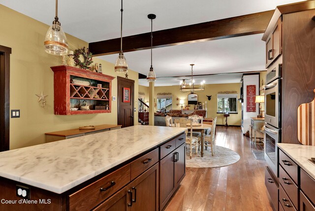 17940 W Sheltered Ct, Hauser, ID 83854 - kitchen featuring decorative light fixtures, hardwood / wood-style flooring, beam ceiling, light stone counters, and open floor plan