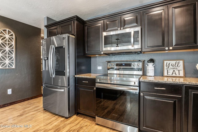 603 Schneiders Rd, Sagle, ID 83860 - kitchen featuring appliances with stainless steel finishes, light wood finished floors, light stone countertops, dark brown cabinets, and a textured ceiling