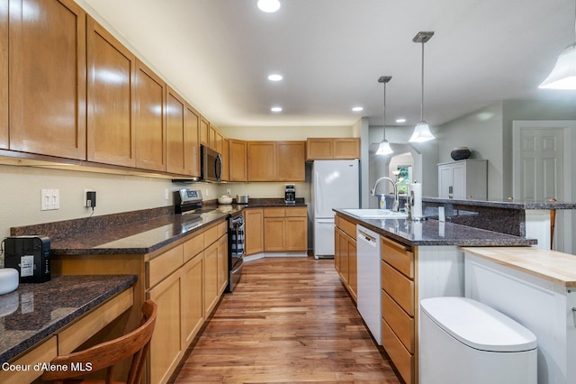 kitchen featuring stainless steel appliances, a sink, light wood finished floors, recessed lighting, and pendant lighting