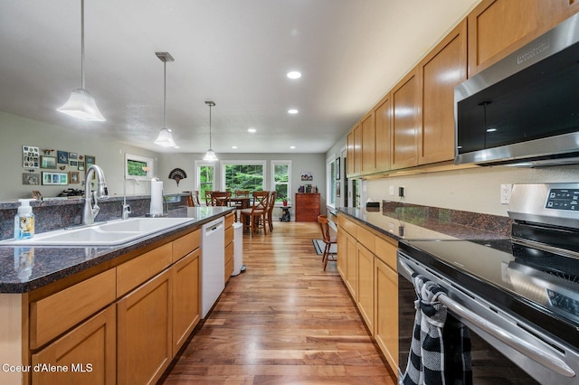 kitchen with appliances with stainless steel finishes, a sink, light wood-style flooring, recessed lighting, and hanging light fixtures