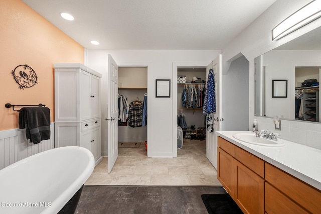 full bath with vanity, a freestanding bath, backsplash, recessed lighting, and a spacious closet