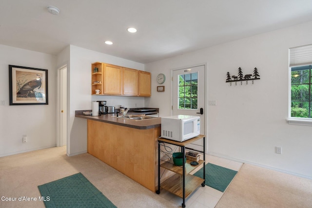 kitchen with white microwave, open shelves, a sink, dark countertops, and a peninsula