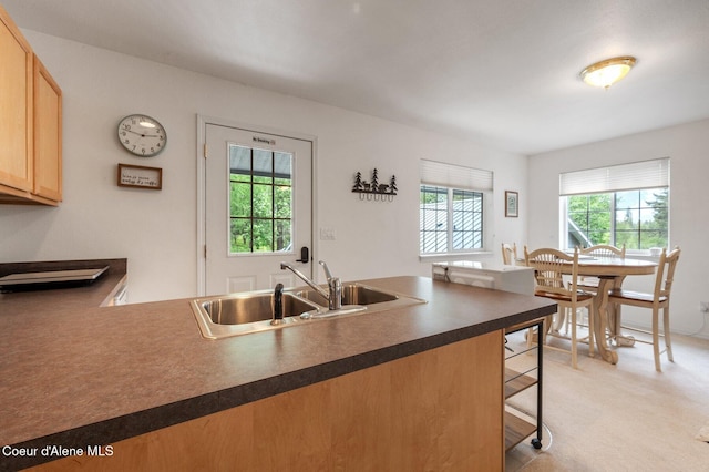 kitchen featuring a sink, dark countertops, a peninsula, a breakfast bar area, and light carpet