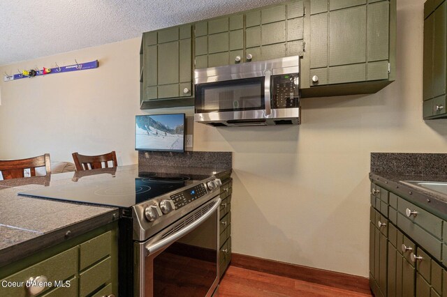 495 NW Psge # 103, Sandpoint, ID 83864 - kitchen featuring appliances with stainless steel finishes, green cabinetry, dark wood-style flooring, dark countertops, and a textured ceiling