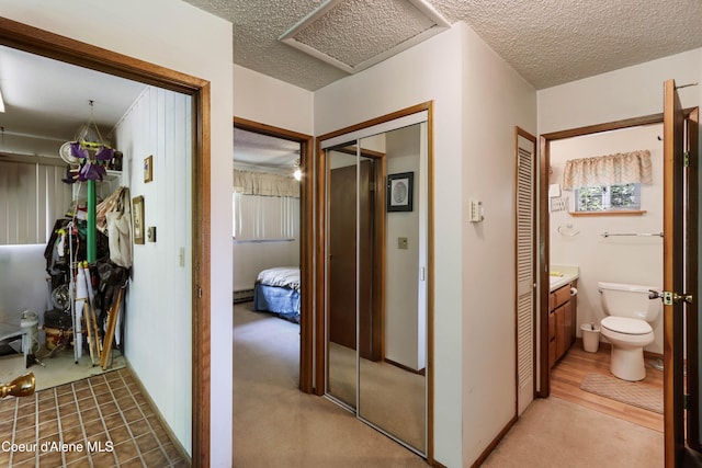 hallway with light carpet, a textured ceiling, attic access, and baseboards