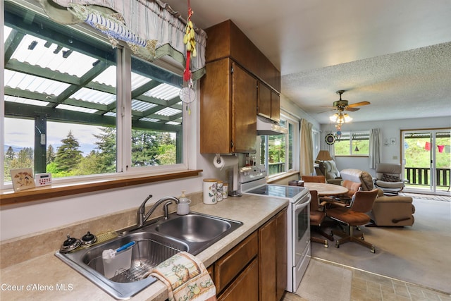 kitchen featuring white range with electric stovetop, a sink, brown cabinetry, plenty of natural light, and a textured ceiling
