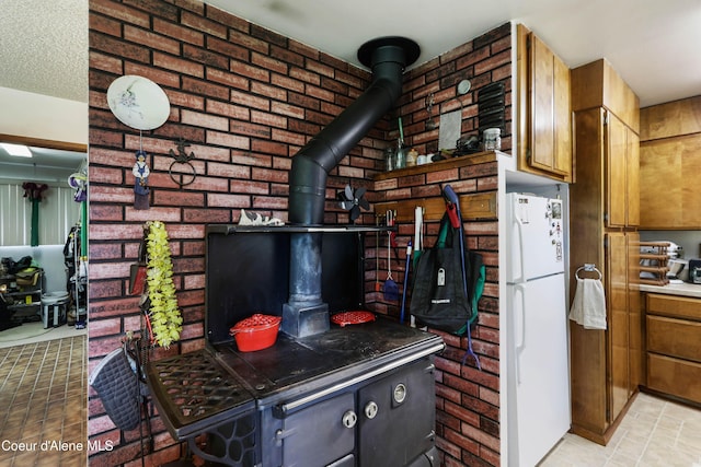 kitchen with freestanding refrigerator, a wood stove, brick wall, and brown cabinetry