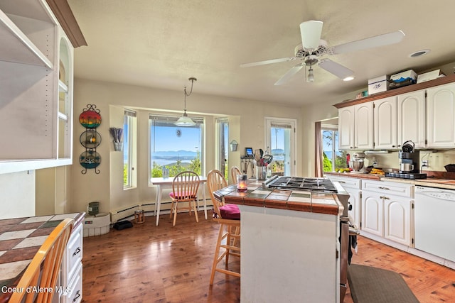 kitchen featuring tile counters, white dishwasher, white cabinetry, ceiling fan, and a breakfast bar