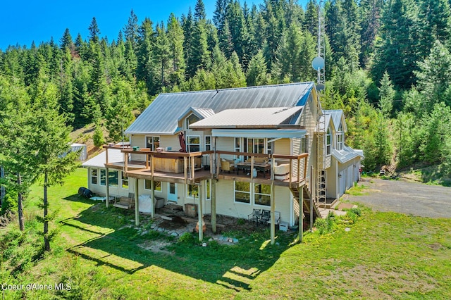 rear view of property with a forest view, driveway, a lawn, metal roof, and a garage