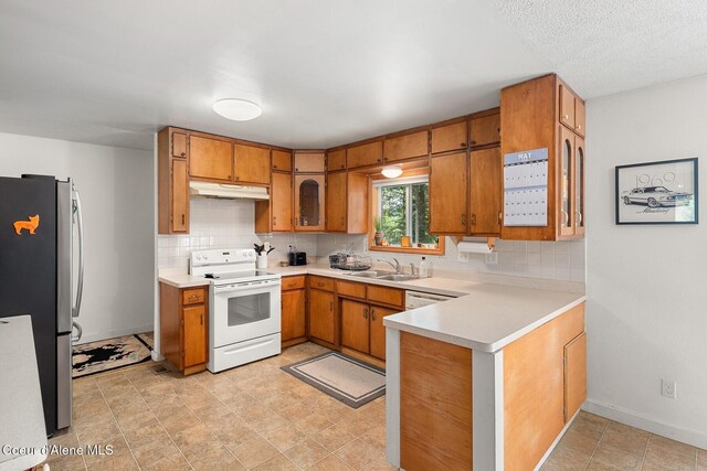 42 Bodie Ln, Priest River, ID 83856 - kitchen with white electric range oven, freestanding refrigerator, under cabinet range hood, a sink, and brown cabinets