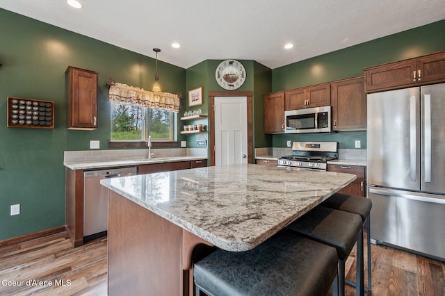 29264 N Ramsey Rd, Athol, ID 83801 - kitchen with appliances with stainless steel finishes, a center island, light wood-style flooring, a kitchen bar, and light stone counters
