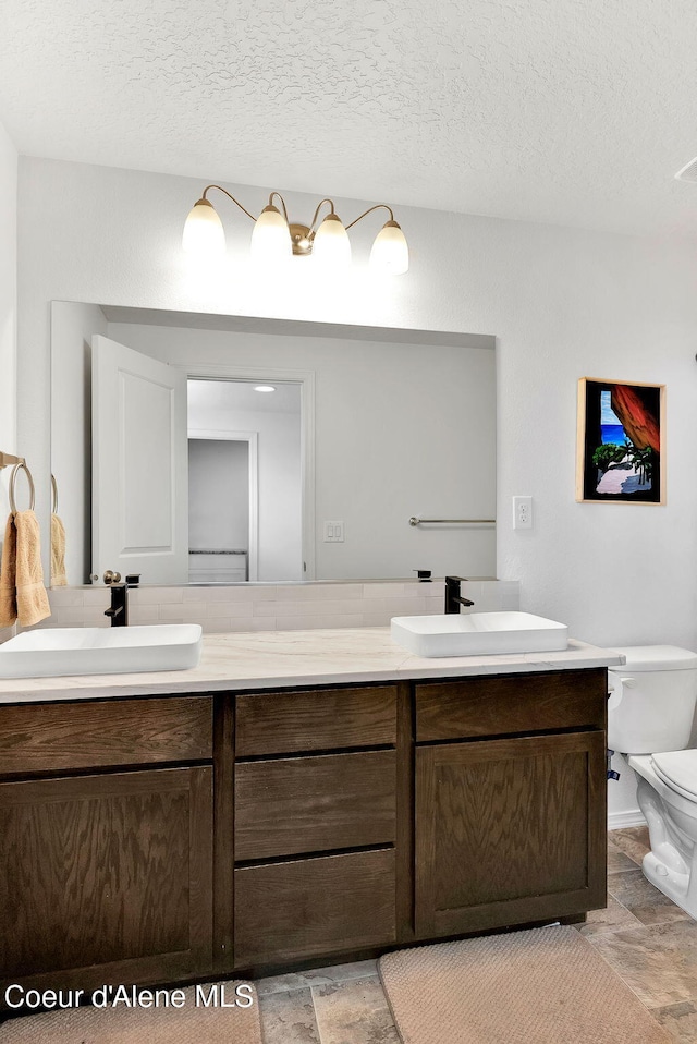 6314 Irish Dr, Rathdrum, ID 83858 - bathroom featuring double vanity, toilet, stone finish flooring, and a textured ceiling