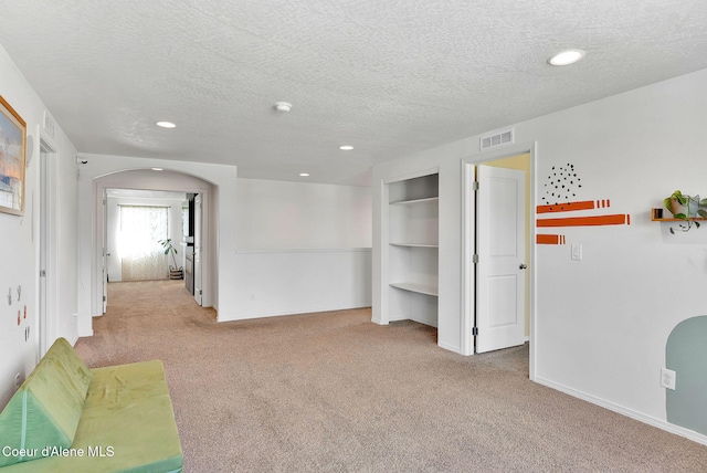 6314 Irish Dr, Rathdrum, ID 83858 - unfurnished living room with carpet, arched walkways, a textured ceiling, built in shelves, and recessed lighting