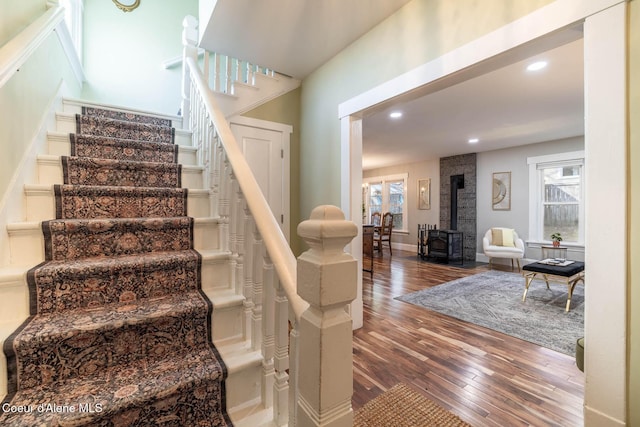 staircase featuring a wood stove, wood-type flooring, plenty of natural light, and recessed lighting