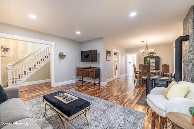 living area featuring stairs, a chandelier, wood finished floors, baseboards, and a wood stove