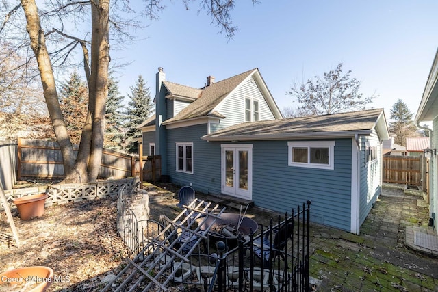 rear view of house featuring french doors, a chimney, a fenced backyard, and a shingled roof