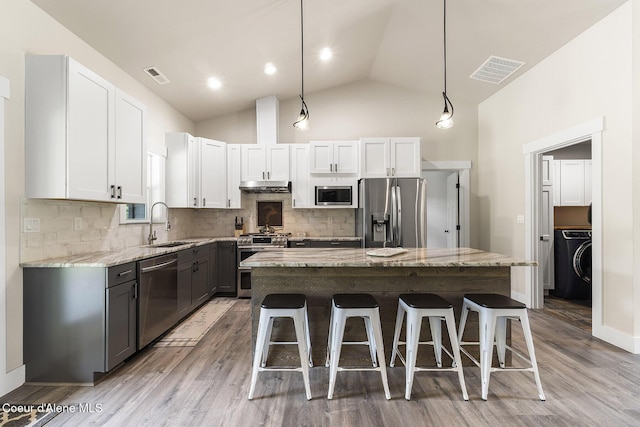 193 Grouse Rd, Sandpoint, ID 83864 - kitchen with appliances with stainless steel finishes, under cabinet range hood, washer / clothes dryer, a kitchen breakfast bar, and high vaulted ceiling