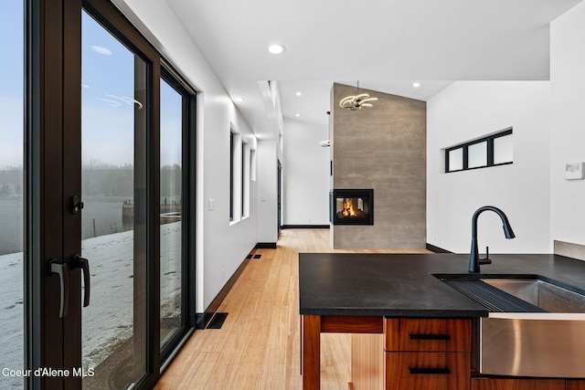 1808 Garfield Bay Rd, Sagle, ID 83860 - kitchen with light wood-style floors, modern cabinets, a multi sided fireplace, a sink, and dark countertops