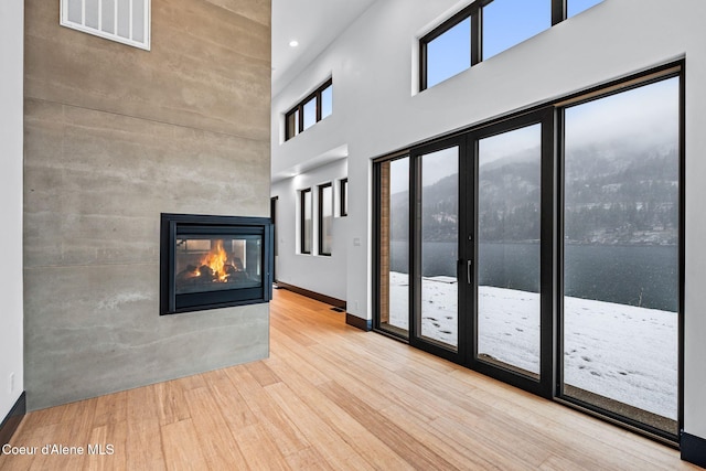 1808 Garfield Bay Rd, Sagle, ID 83860 - unfurnished living room featuring wood finished floors, a high ceiling, a multi sided fireplace, baseboards, and recessed lighting