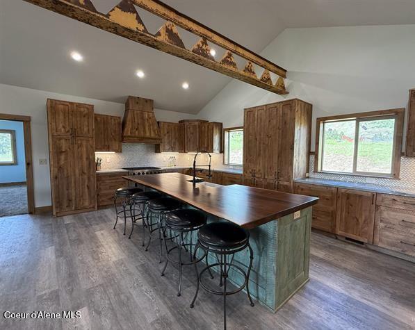240 Canyon Dr, Kooskia, ID 83539 - kitchen with custom exhaust hood, vaulted ceiling, brown cabinets, a center island with sink, and a kitchen bar