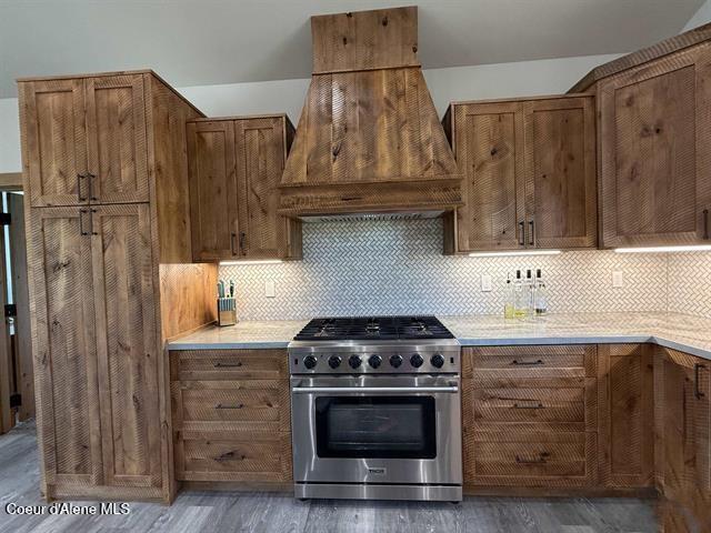 240 Canyon Dr, Kooskia, ID 83539 - kitchen with stainless steel stove, custom range hood, brown cabinetry, wood finished floors, and decorative backsplash