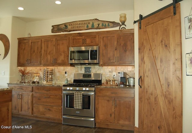 995 S Saddleback Dr, Coeur Dalene, ID 83814 - kitchen with stainless steel appliances, dark stone countertops, backsplash, a barn door, and recessed lighting