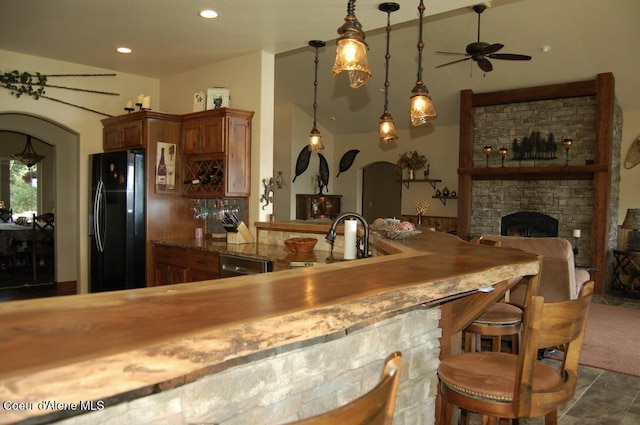 995 S Saddleback Dr, Coeur Dalene, ID 83814 - kitchen with freestanding refrigerator, arched walkways, a ceiling fan, brown cabinetry, and a fireplace