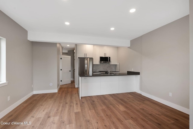 1670 Onyx Ct, Sandpoint, ID 83864 - kitchen with appliances with stainless steel finishes, a peninsula, decorative backsplash, dark countertops, and light wood-type flooring
