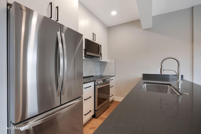 1670 Onyx Ct, Sandpoint, ID 83864 - kitchen featuring appliances with stainless steel finishes, a sink, dark countertops, light wood-style flooring, and white cabinets
