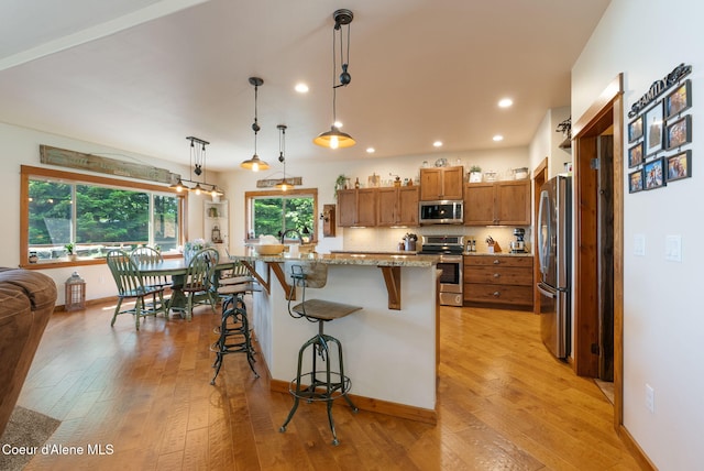 17378 N Freddi Rd, Rathdrum, ID 83858 - kitchen with appliances with stainless steel finishes, brown cabinetry, light wood-style floors, a breakfast bar area, and light stone countertops