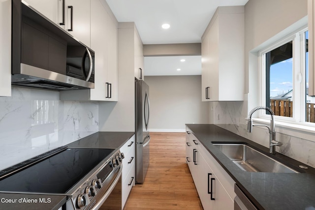 1674 Onyx Ct, Sandpoint, ID 83864 - kitchen featuring stainless steel appliances, a sink, dark countertops, light wood-type flooring, and white cabinets
