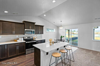 13659 N Apex Way, Hayden, ID 83835 - kitchen with appliances with stainless steel finishes, lofted ceiling, light countertops, dark brown cabinetry, and a kitchen bar