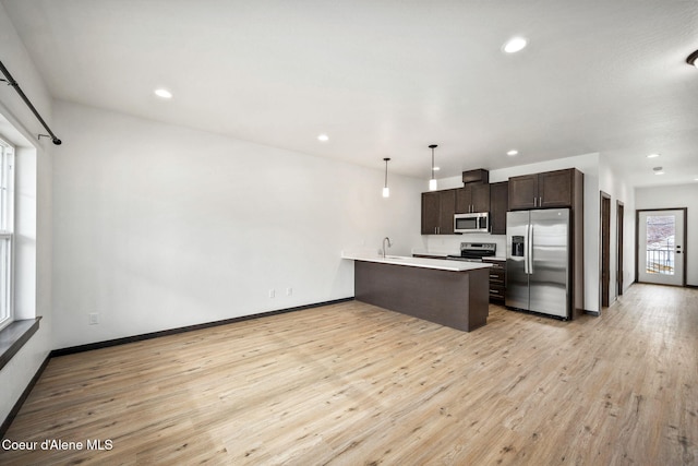2248 N Syringa St, Post Falls, ID 83854 - kitchen featuring appliances with stainless steel finishes, a peninsula, dark brown cabinets, light countertops, and light wood-style flooring