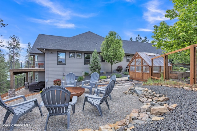 4618 S Scenic Dr, Coeur Dalene, ID 83814 - back of property featuring a greenhouse, an outdoor fire pit, a balcony, a shingled roof, and an outdoor structure
