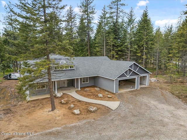 10233 Bunco Rd, Athol, ID 83801 - view of front of house featuring an attached garage, dirt driveway, covered porch, a forest view, and roof with shingles