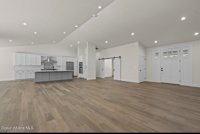10233 Bunco Rd, Athol, ID 83801 - unfurnished living room featuring vaulted ceiling, a barn door, light wood-type flooring, and recessed lighting