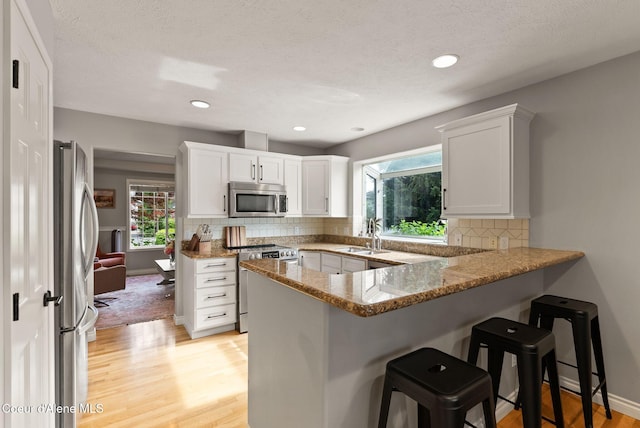 5030 E Frazier Dr, Post Falls, ID 83854 - kitchen featuring appliances with stainless steel finishes, a peninsula, a sink, a kitchen bar, and light wood-style flooring