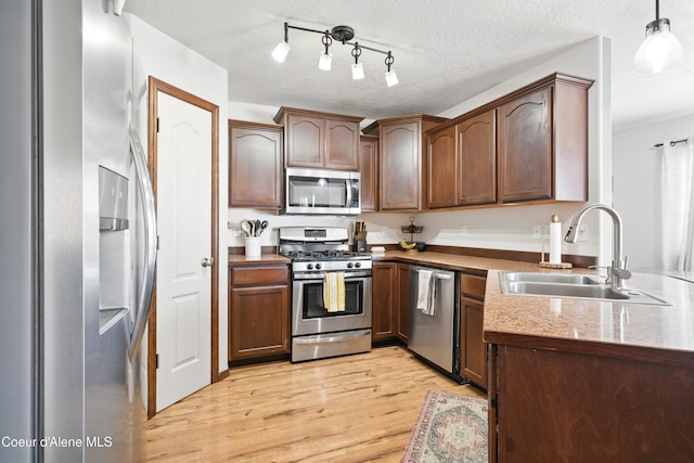 12404 W Devonshire Ave, Post Falls, ID 83854 - kitchen with appliances with stainless steel finishes, a sink, light wood-style floors, pendant lighting, and a textured ceiling