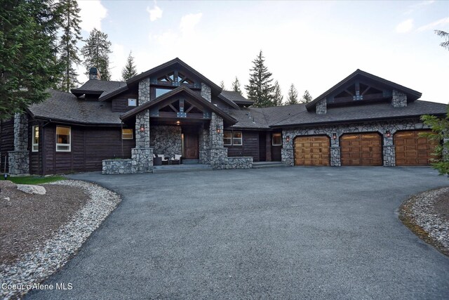 225 Fairway Dr, Priest Lake, ID 83856 - view of front of home with stone siding, asphalt driveway, an attached garage, and a chimney