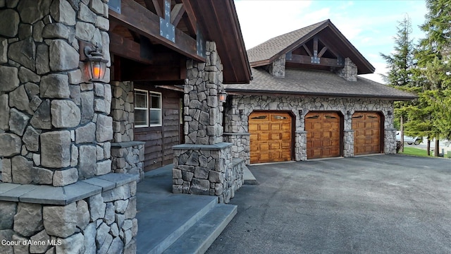225 Fairway Dr, Priest Lake, ID 83856 - view of side of home featuring stone siding, a shingled roof, and asphalt driveway