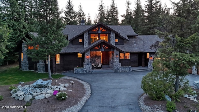 225 Fairway Dr, Priest Lake, ID 83856 - view of front of home with stone siding, a shingled roof, driveway, and a chimney