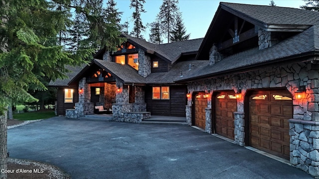 225 Fairway Dr, Priest Lake, ID 83856 - view of front of property featuring stone siding, asphalt driveway, a porch, and roof with shingles