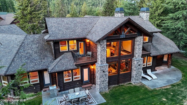225 Fairway Dr, Priest Lake, ID 83856 - rear view of house with stone siding, a chimney, a patio, and roof with shingles