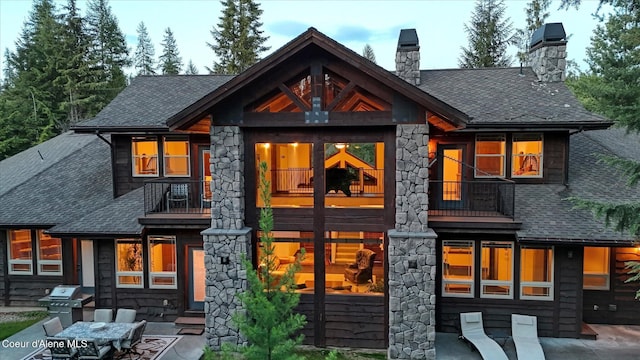 225 Fairway Dr, Priest Lake, ID 83856 - rear view of property featuring a balcony, a chimney, a shingled roof, and stone siding