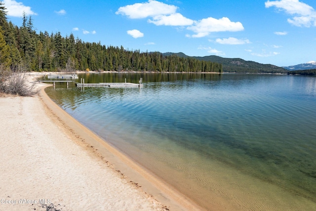 225 Fairway Dr, Priest Lake, ID 83856 - water view featuring a boat dock, a heavily wooded area, and a mountain backdrop